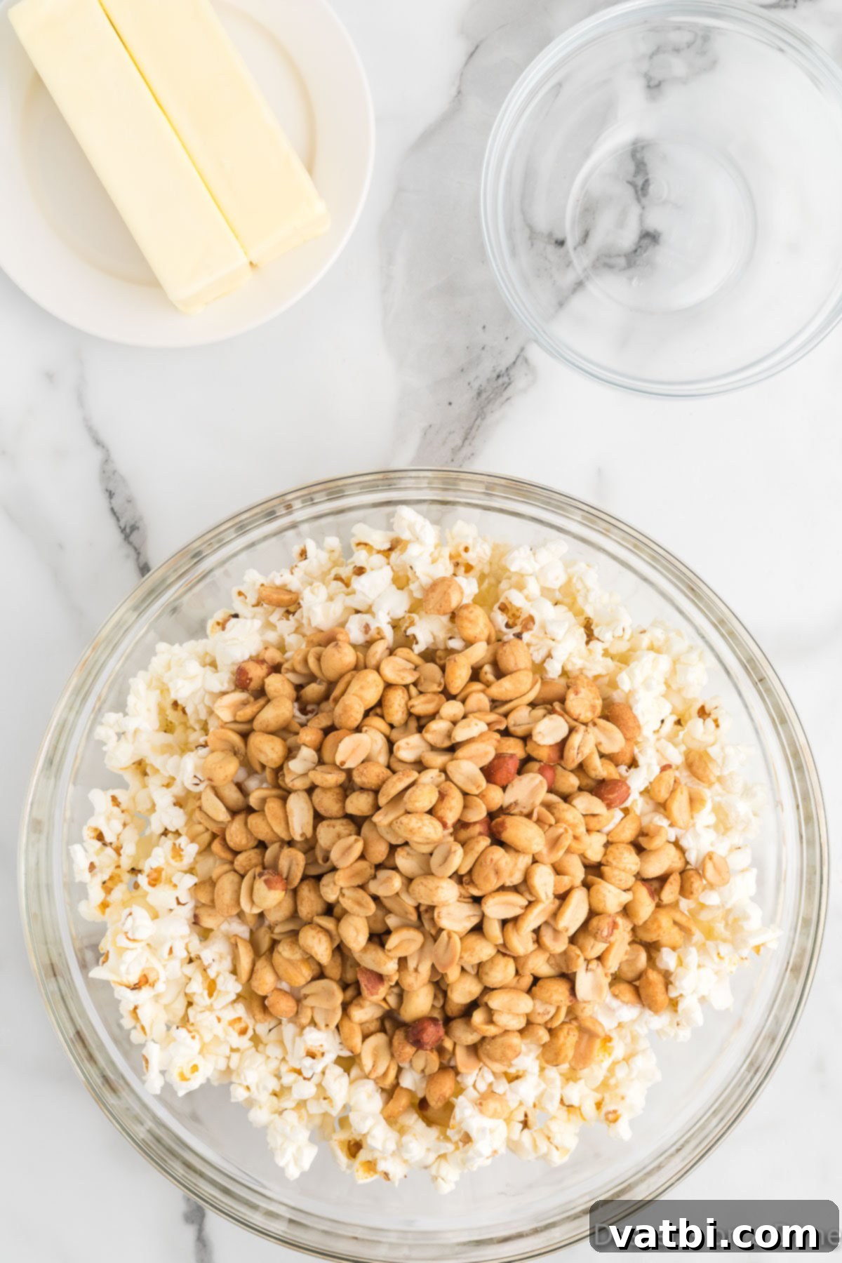 Buttery Toffee Bliss Popcorn 5 Peanuts being stirred into a bowl of popped popcorn.