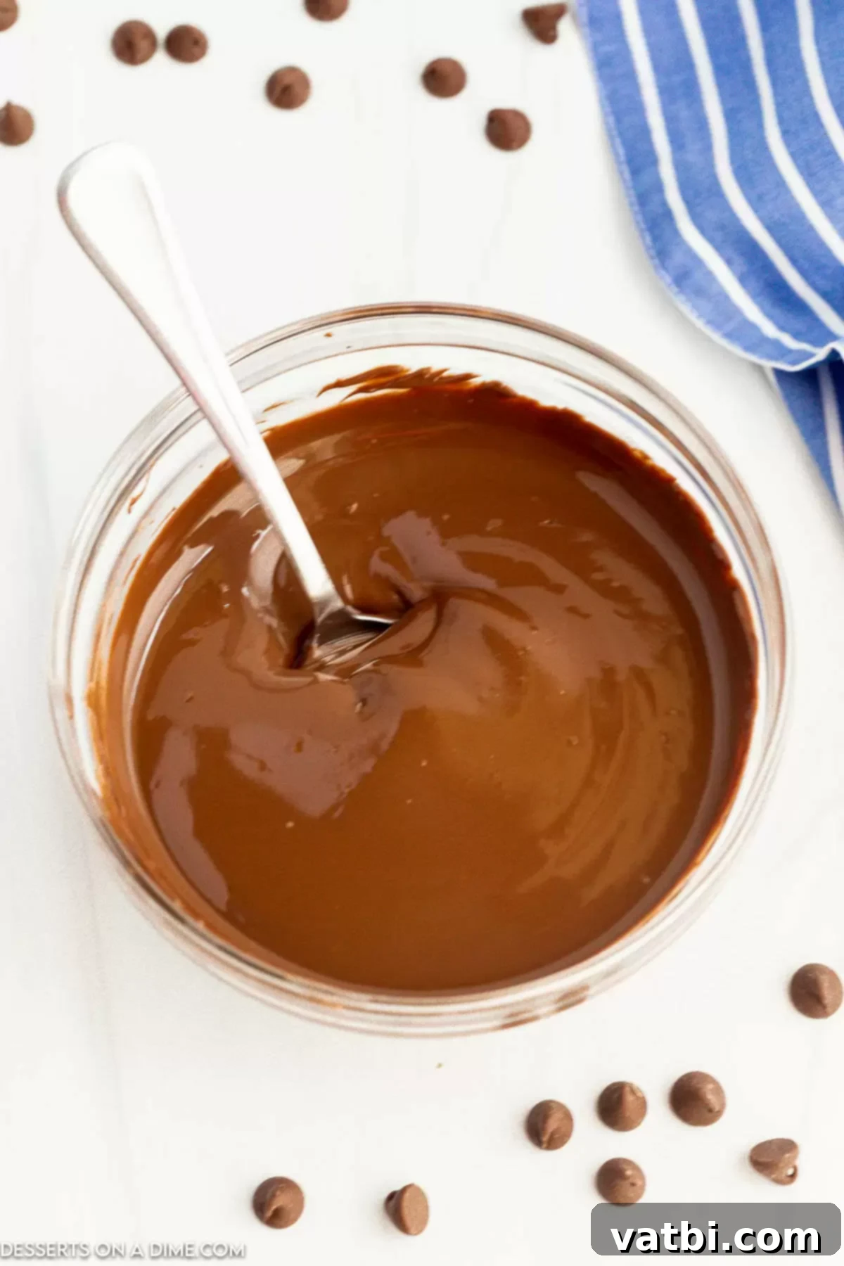 Melt Chocolate Chips Perfectly Every Time 5 Melted chocolate in a clear bowl with a spoon, demonstrating a perfect, smooth consistency achieved through careful melting.