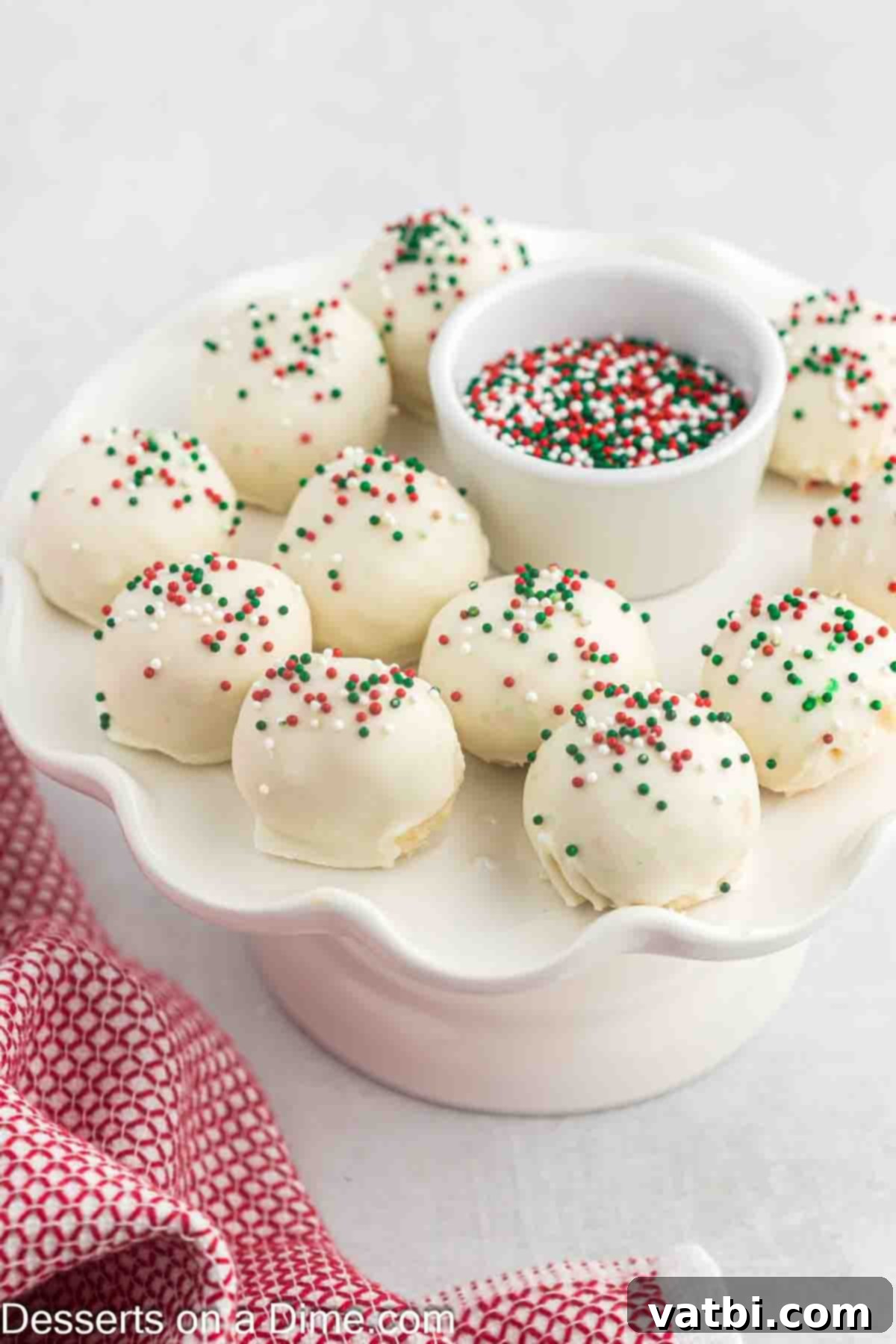 sugar cookie truffles on a cake platter with a bowl of sprinkles