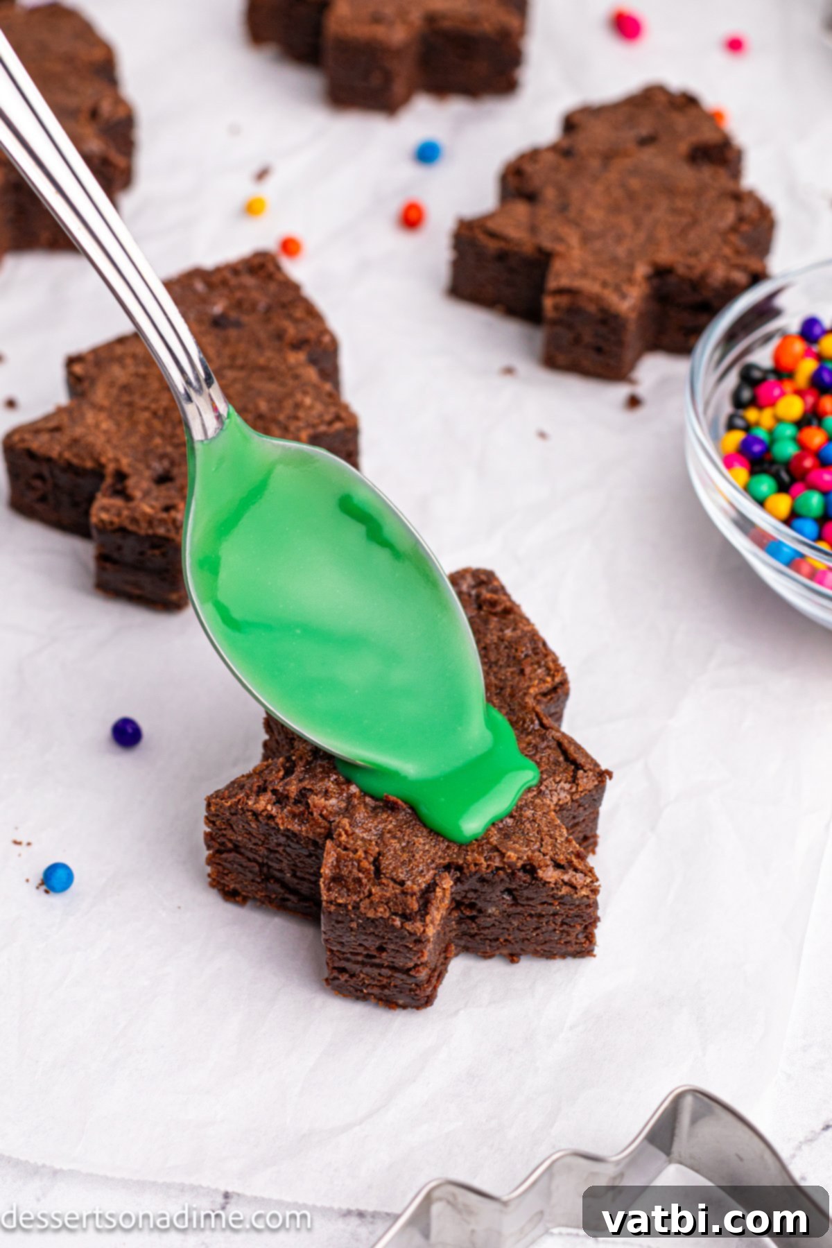 Little Debbie Inspired Christmas Tree Brownies 9 A spoon drizzling the green melted candy topping over each Christmas tree brownie, ensuring even coverage.