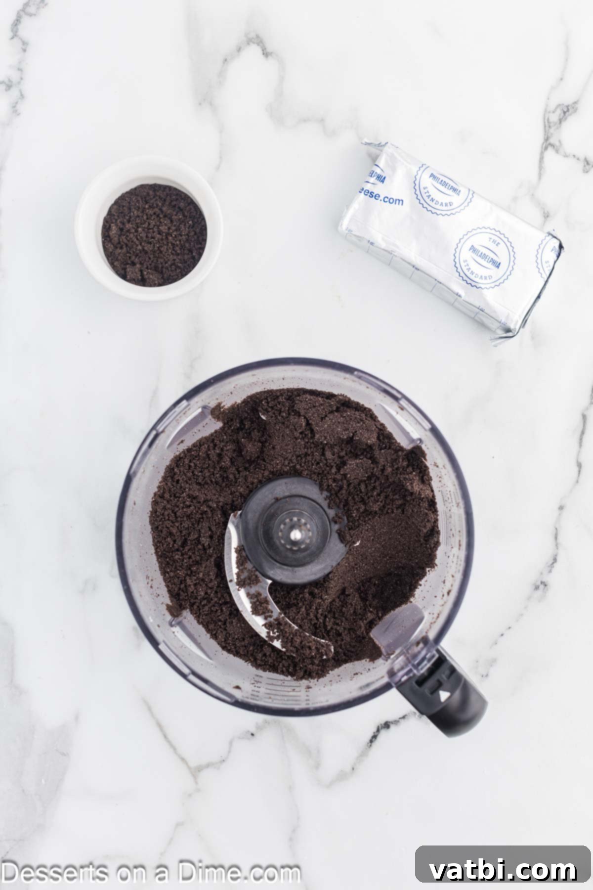 Oreo cookies are being finely crushed in a food processor, transforming them into a uniform crumb texture, ready for mixing.