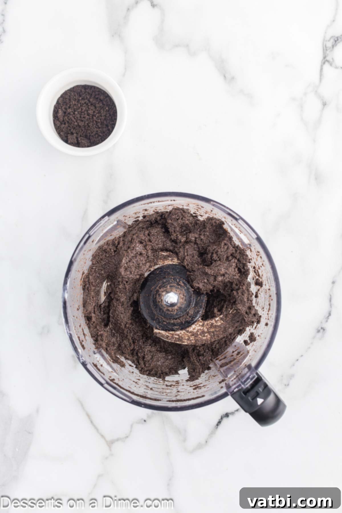 Softened cream cheese is being blended with the crushed Oreo cookie crumbs in a food processor, creating a cohesive, dark mixture for the cake pops.