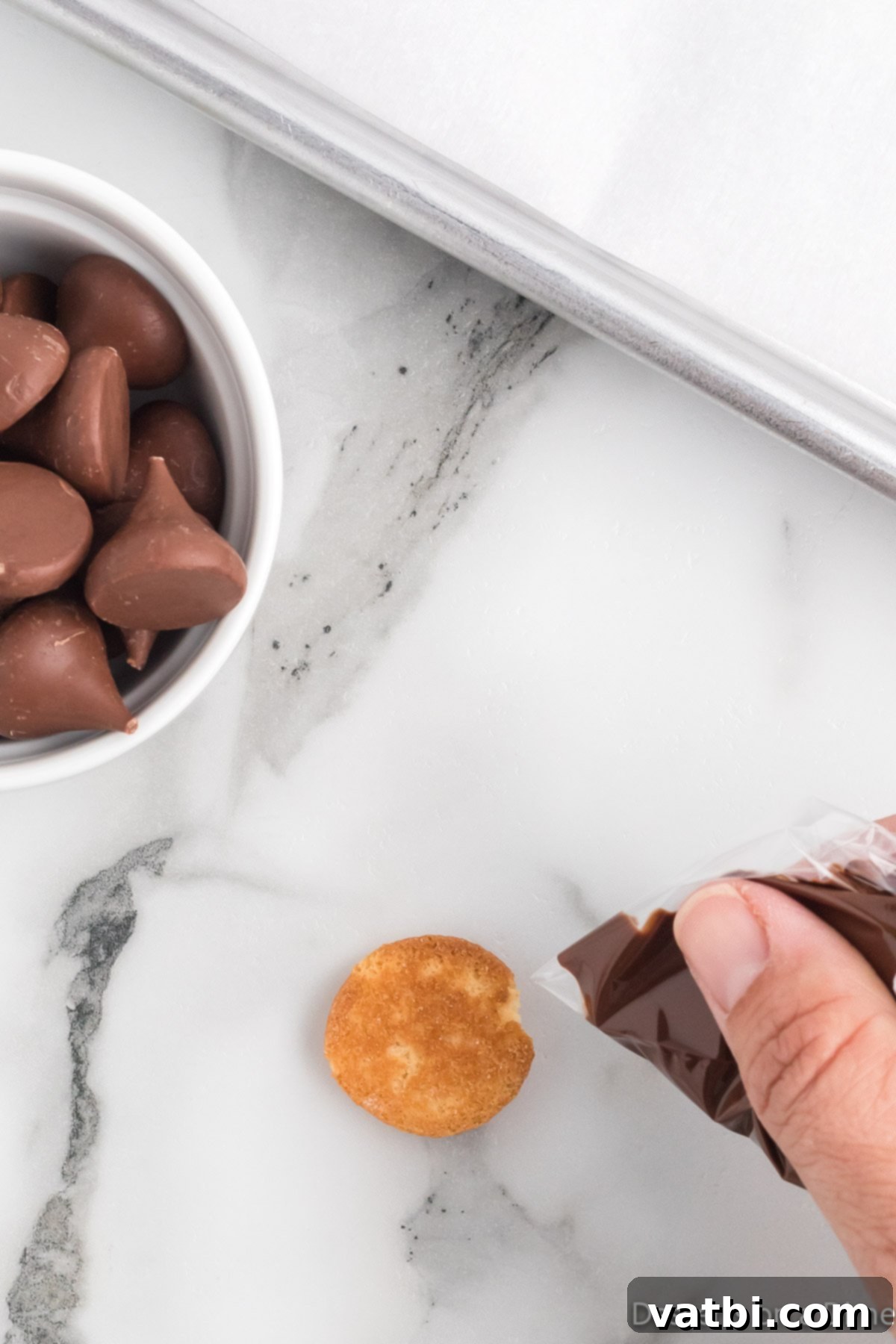 Melted chocolate in a ziploc bag being piped on to a vanilla wafer. 