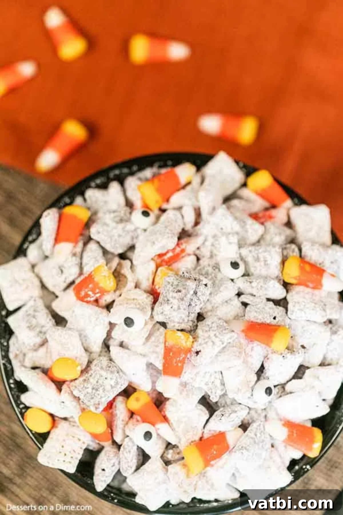 The kids will go crazy over this Halloween puppy chow recipe and it is so easy. Halloween muddy buddies puppy chow looks so festive with candy corn, candy eyes and more. Halloween Muddy Buddies is a delicious chex mix recipe. #dessertonadime #halloweenpuppychowrecipe #glutenfree Halloween Puppy Chow in a black bowl, decorated with candy corn and candy eyes.