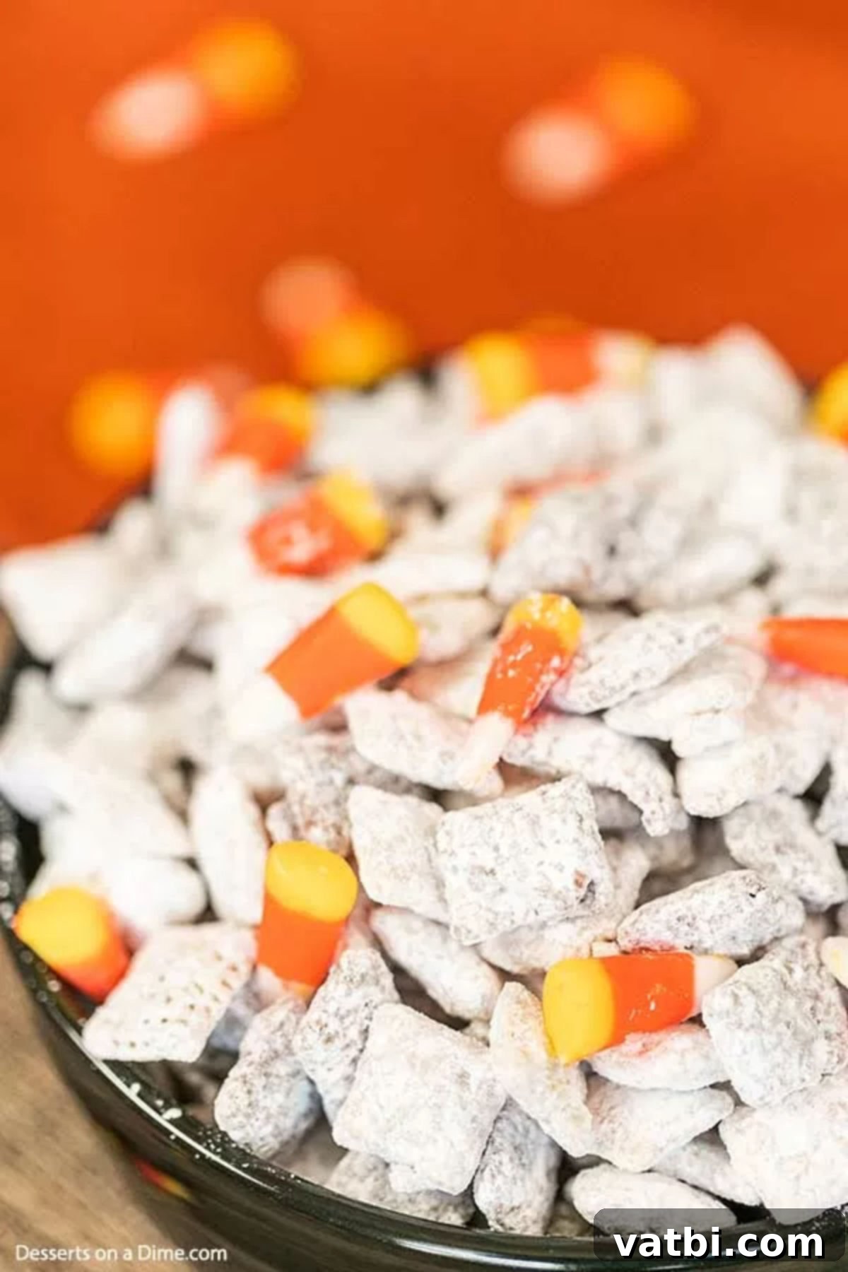 The kids will go crazy over this Halloween puppy chow recipe and it is so easy. Halloween muddy buddies puppy chow looks so festive with candy corn, candy eyes and more. Halloween Muddy Buddies is a delicious chex mix recipe. #dessertonadime #halloweenpuppychowrecipe #glutenfree Halloween Puppy Chow in a black bowl, closeup.