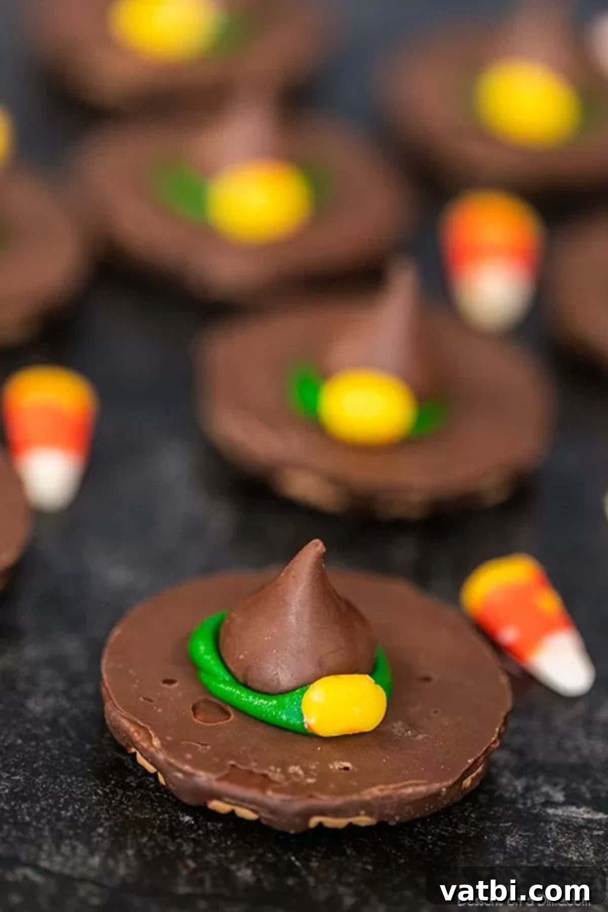 Witch hat cookies are the perfect no bake treat and they are easy to make for Halloween with hershey kisses. Halloween witch hat cookies decorated make the cutest treat for parties and more. #dessertonadime #witchhatcookies #harrypotter Halloween Witch Hat Cookies with vibrant green icing and candy corn buckles, presented on a platter with extra candy corn.