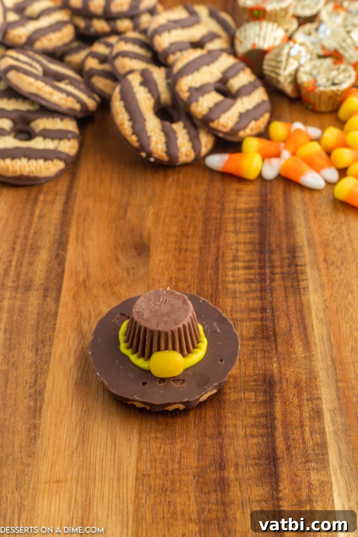 Orange piece of candy corn attached to the front of the Reese's cup, on the yellow icing brim, acting as a decorative buckle.