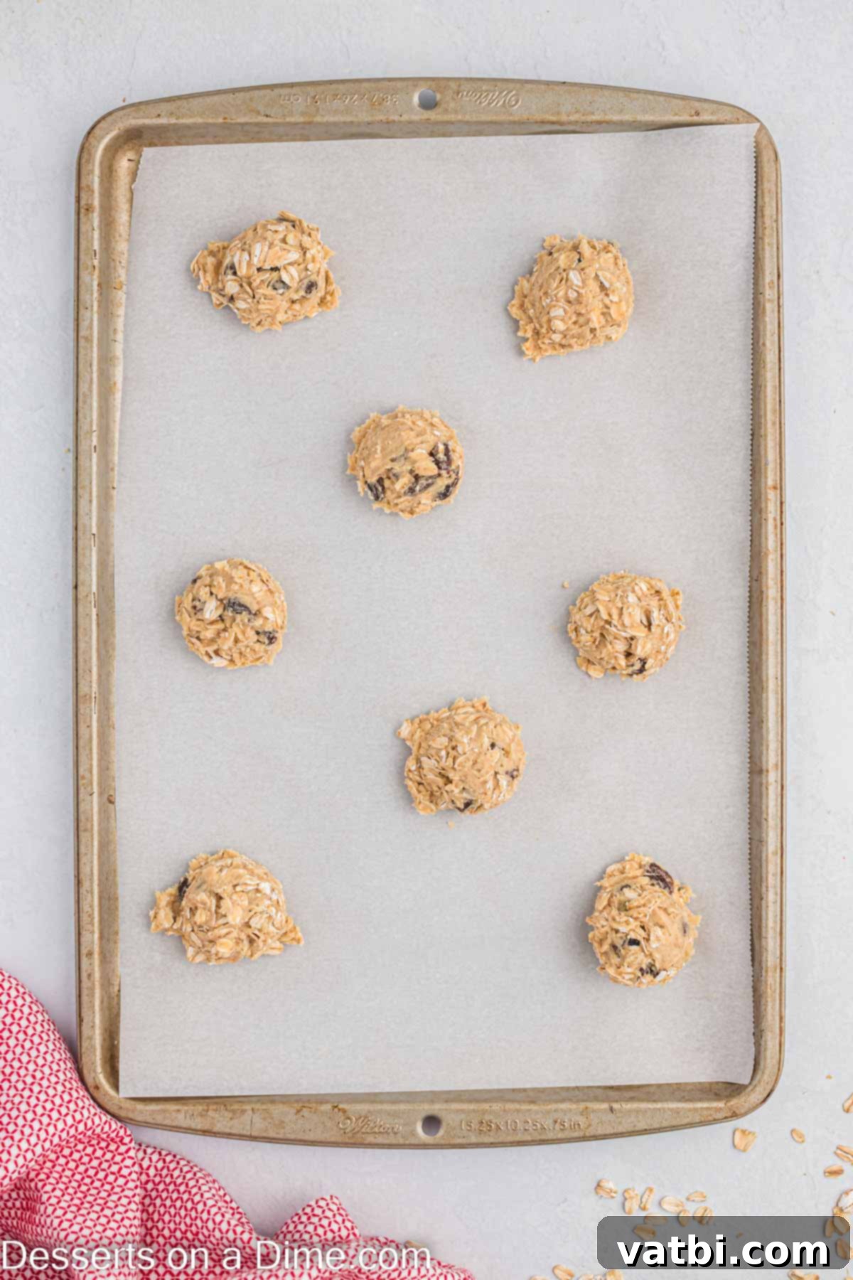 Chewy Oatmeal Raisin Cookie Perfection 5 Uniformly portioned cookie dough balls resting on a parchment-lined baking sheet, ready to be baked.