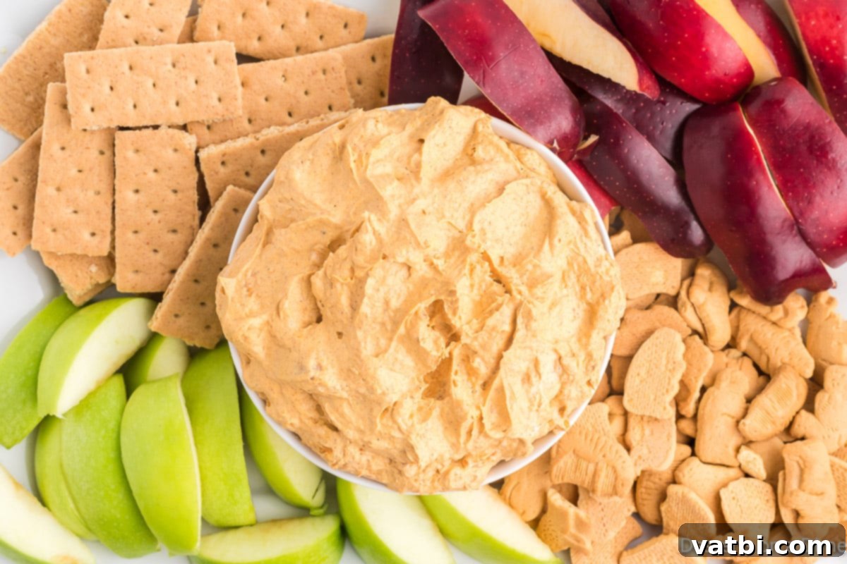Fluffy Pumpkin Dessert Dip 2 Creamy Pumpkin Dip with Cool Whip served in a festive bowl, surrounded by various dippers like apple slices, graham crackers, and gingersnaps, perfect for fall gatherings.