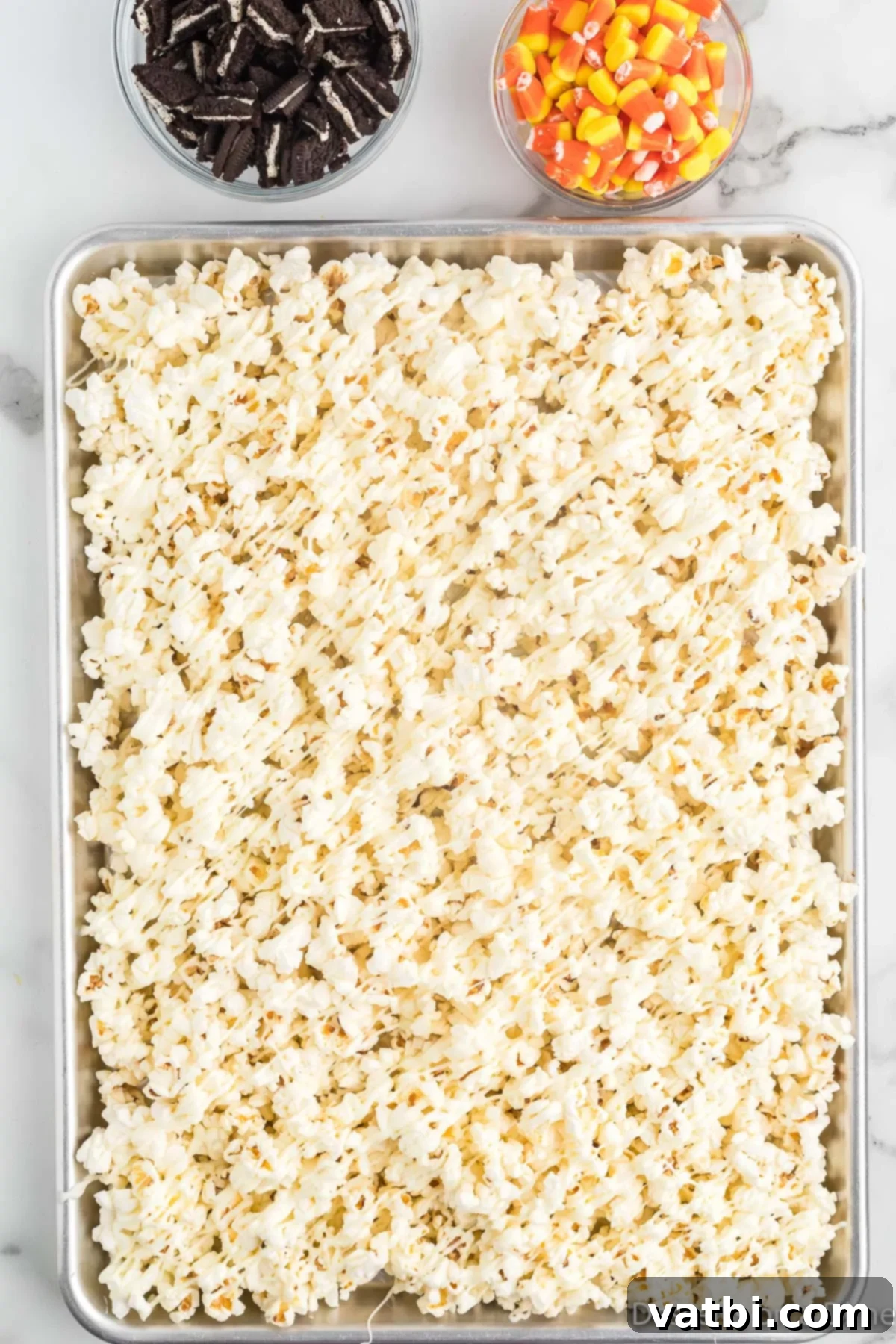 Fright Night Popcorn 6 Drizzling melted white chocolate over the popcorn on a baking sheet.