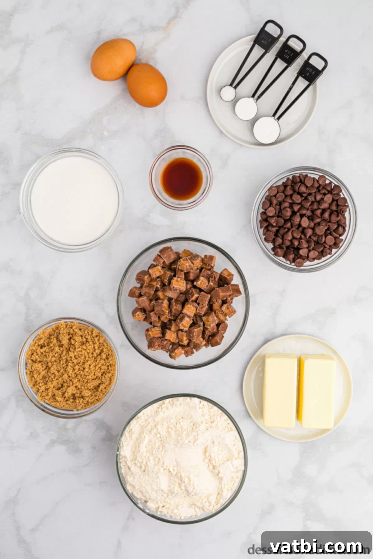 Ingredients laid out for Milky Way Cookies: softened butter, granulated sugar, light brown sugar, large eggs, vanilla extract, all-purpose flour, baking soda, baking powder, salt, chocolate chips, and chopped fun-size Milky Way candy bars.