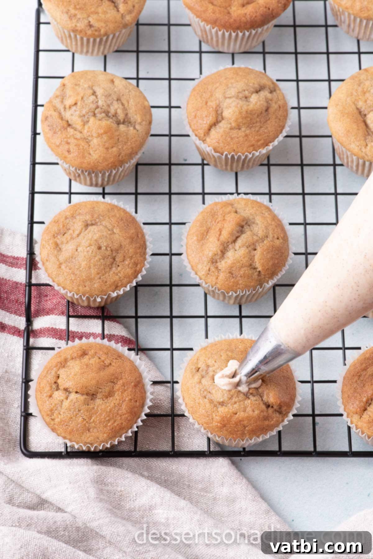 Piping cinnamon cream cheese frosting onto fully cooled churro cupcakes using a star tip, then topping with churro pieces.