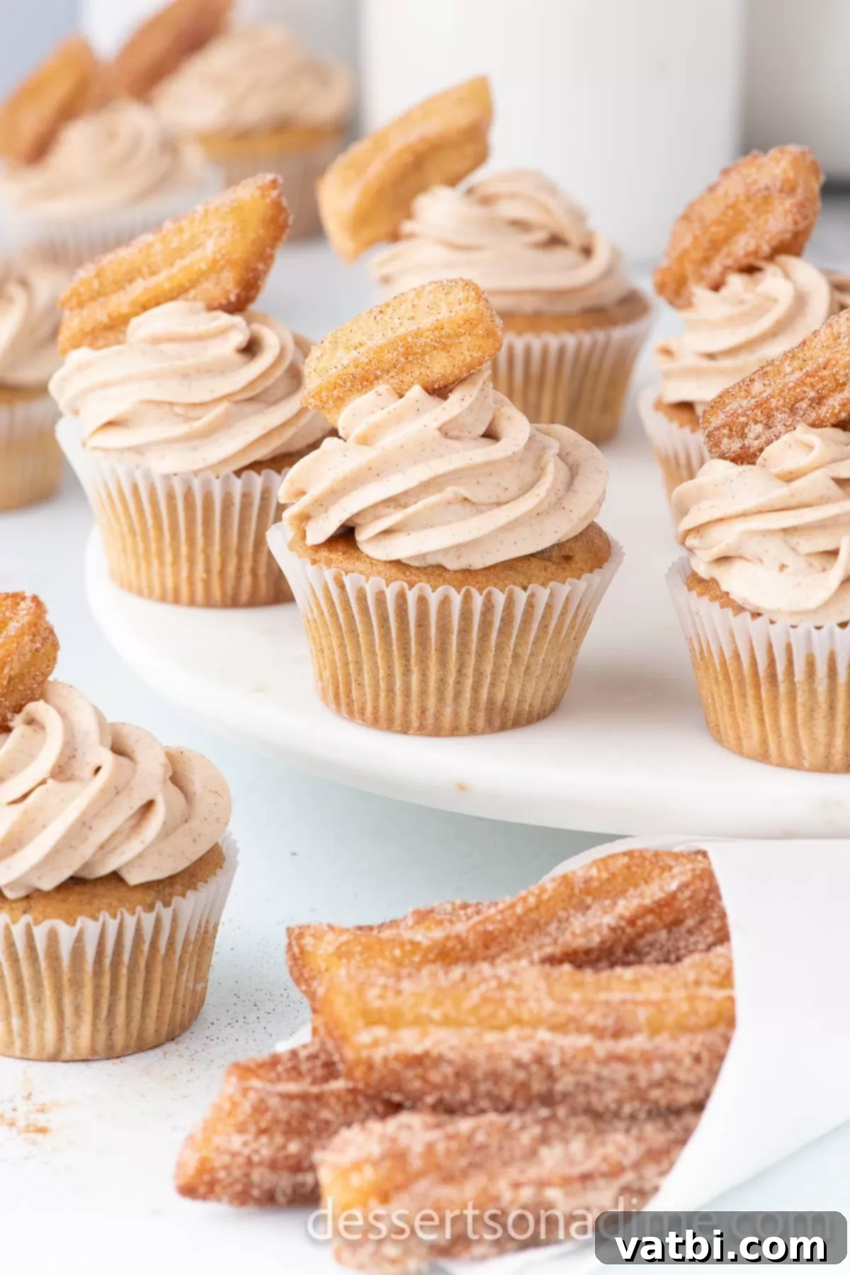A close-up view of a frosted Churro Cupcake, adorned with a piece of churro and a dusting of cinnamon sugar.