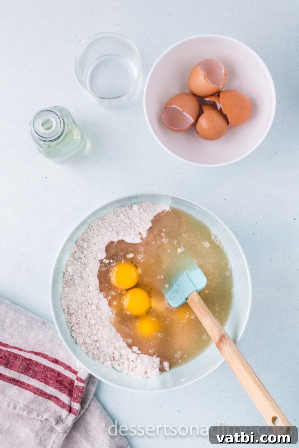 Stirring in large eggs, vegetable oil, and warm water into the bowl of dry ingredients for the cupcake batter.