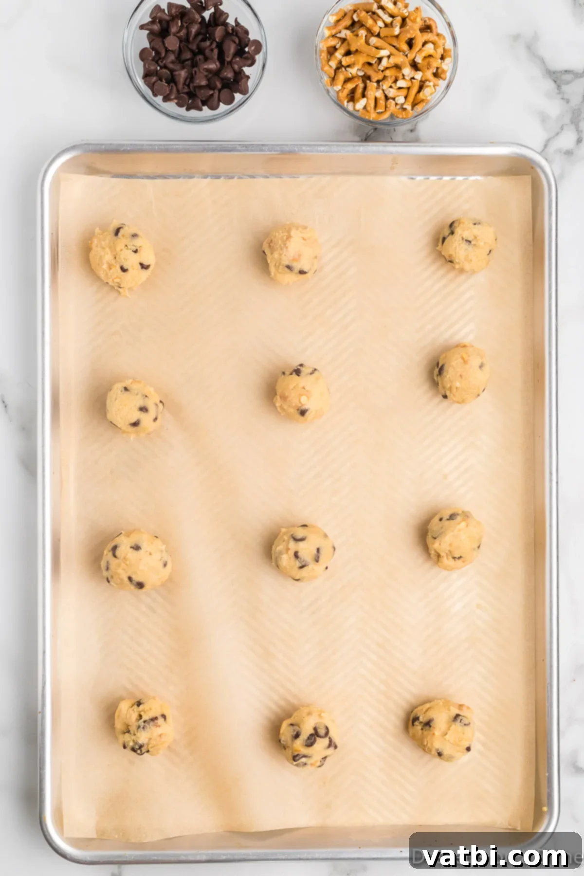 Salty Sweet Chocolate Pretzel Crunch 10 Scoops of cookie dough arranged on a parchment-lined baking sheet, ready for baking.