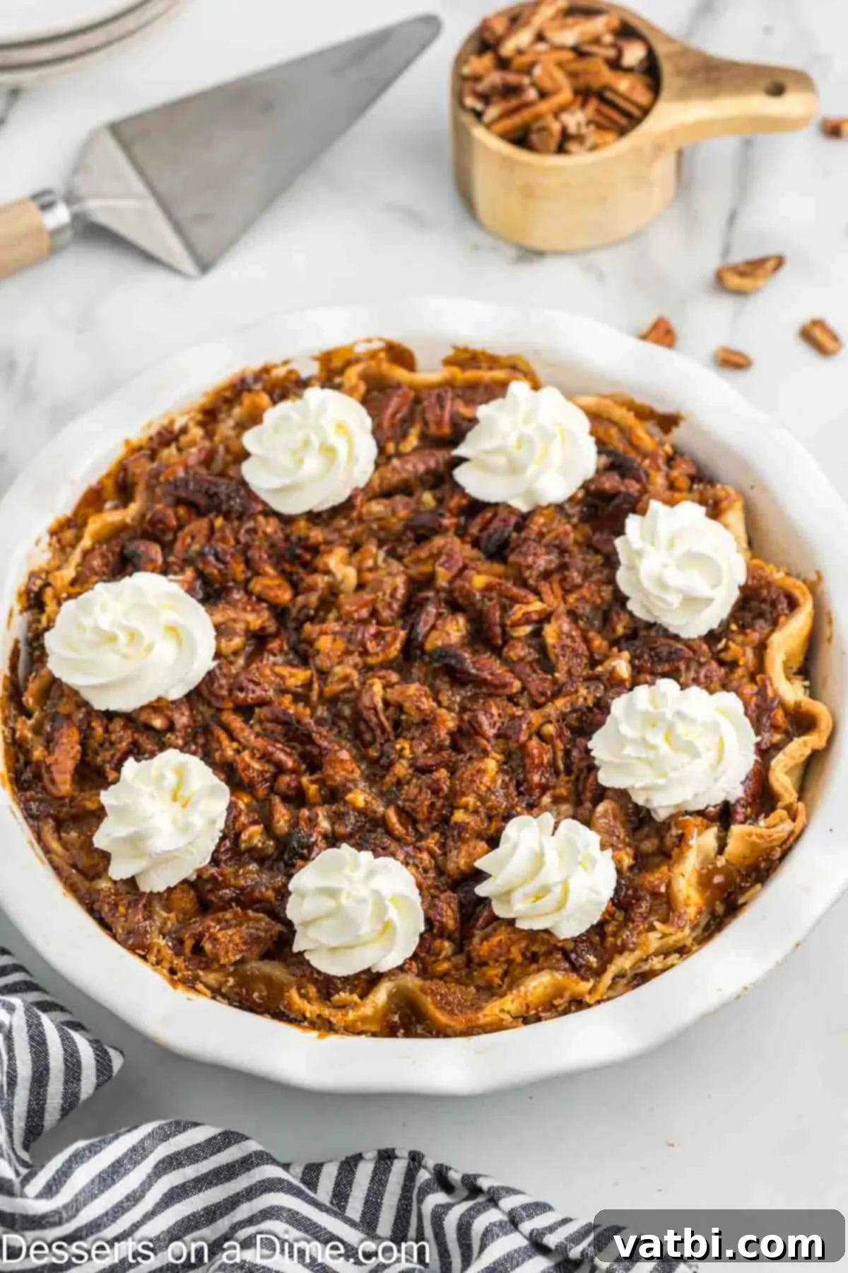 Southern Sweet Potato Pecan Pie 2 Whole Sweet Potato Pecan Pie in a pie dish topped with a dollop of whipped cream and a sprinkle of cinnamon, ready for holiday serving.