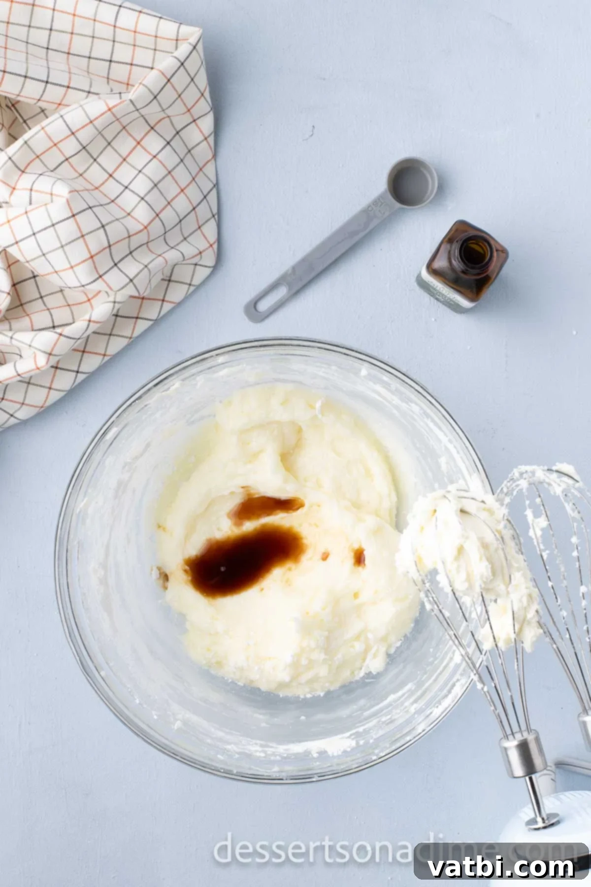 Vanilla extract being added to the cream cheese and butter mixture, enhancing the frosting's flavor.