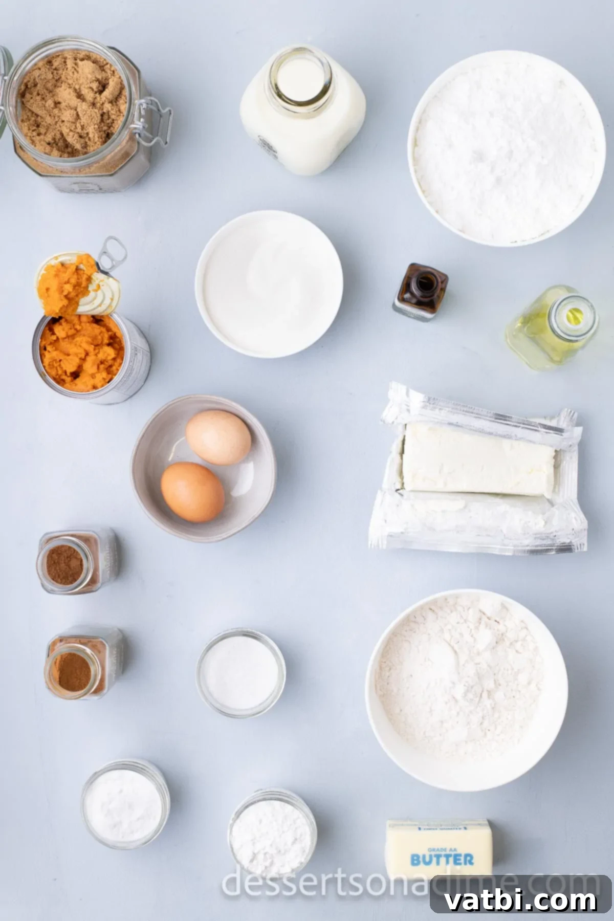 Assorted Pumpkin Cheesecake Cupcake Ingredients including flour, baking soda, pumpkin puree, brown sugar, pumpkin pie spice, butter, vanilla, and cream cheese, laid out on a surface.