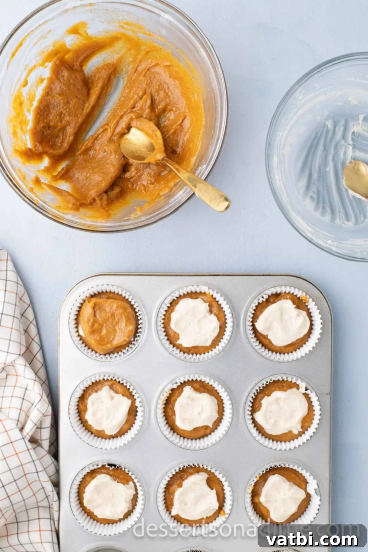Additional pumpkin batter carefully placed on top of the cheesecake filling, covering it completely in each cupcake tin.