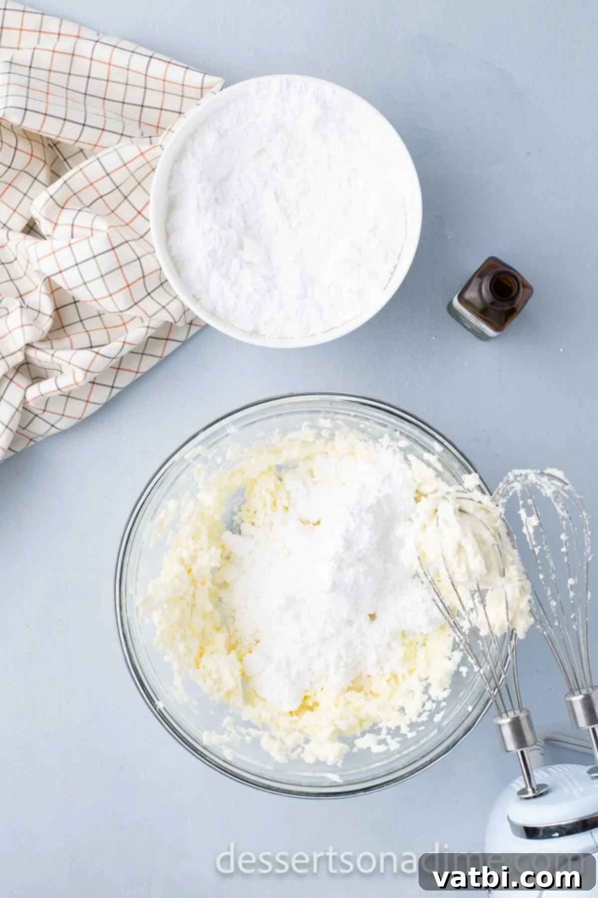 Softened cream cheese and butter are beaten together in a mixing bowl until light and fluffy, forming the base of the frosting.