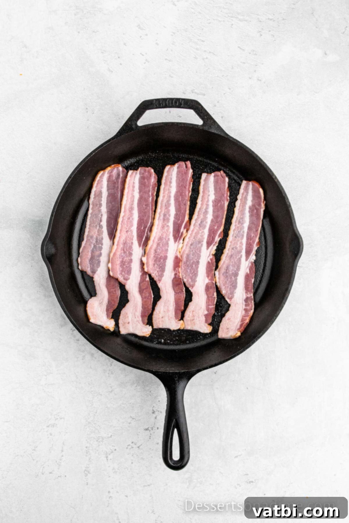 Decadent Bacon Cinnamon Buns 4 A cast iron skillet filled with strips of bacon cooking until crispy and golden brown.