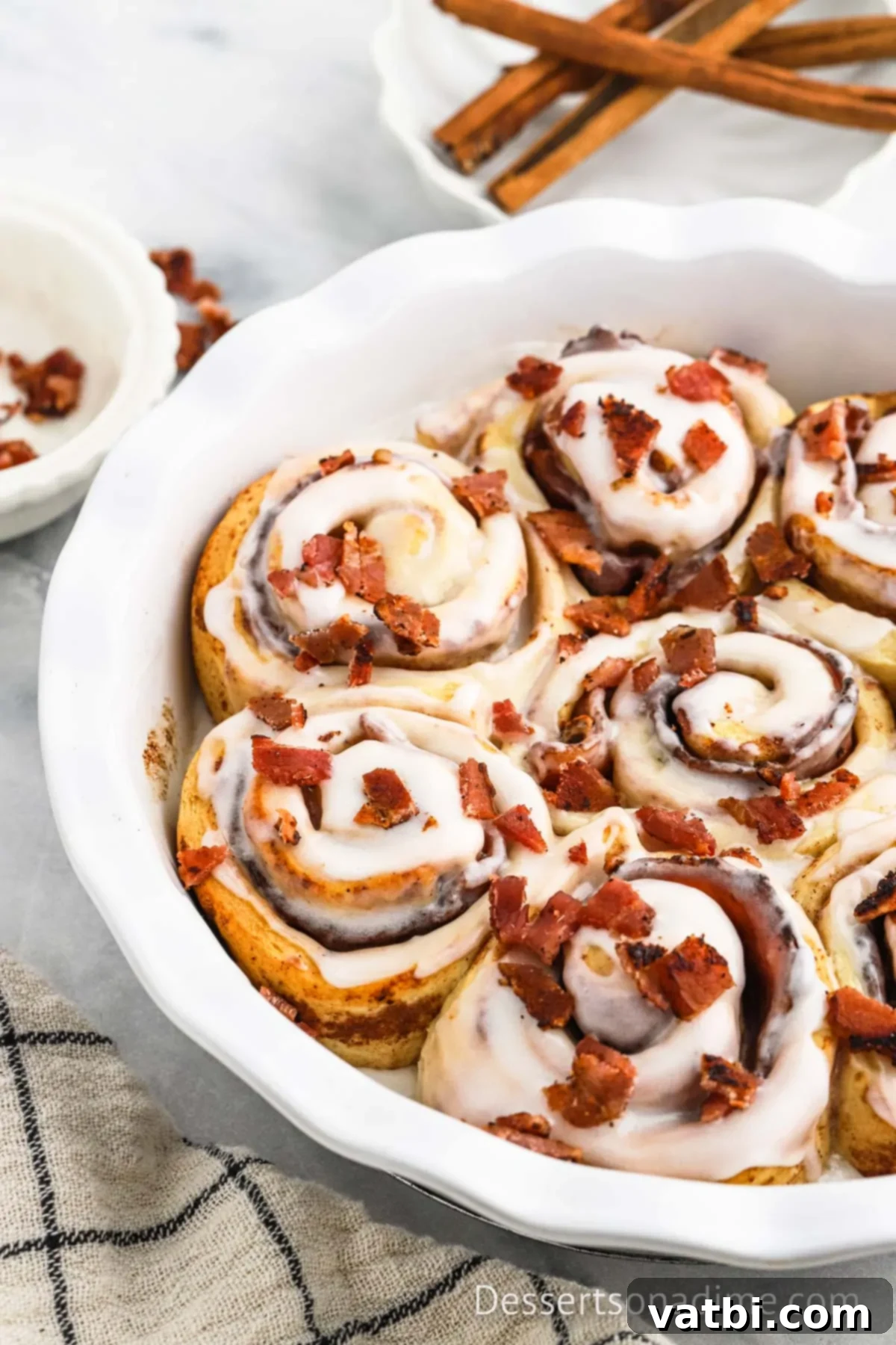 Decadent Bacon Cinnamon Buns 10 A baking dish filled with several golden-brown Bacon Cinnamon Rolls, topped with white icing and scattered bacon bits, ready to be enjoyed.