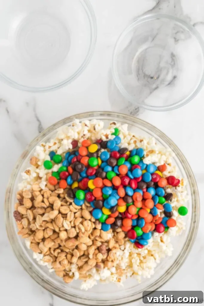 Homemade Popcorn Delight Bars 4 A large mixing bowl filled with freshly popped popcorn, salted peanuts, and colorful M&M's, ready for the marshmallow mixture.