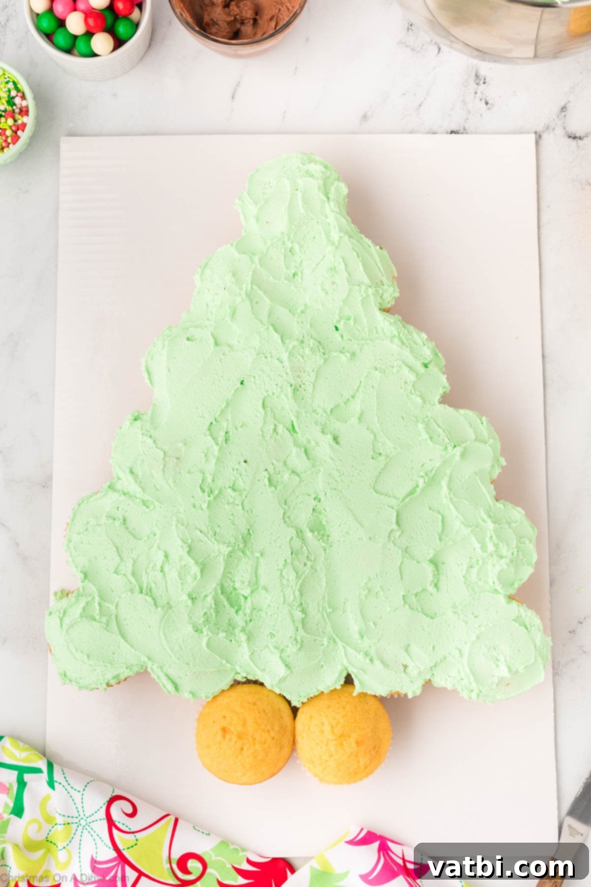 Green frosting being smoothly spread across the arranged cupcakes to create a continuous surface, resembling a single cake.