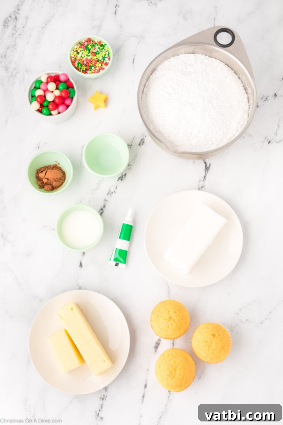 A collection of ingredients for Christmas Tree Cupcakes including vanilla cupcakes, butter, vanilla extract, powdered sugar, milk, green food coloring, cocoa powder, and festive sprinkles.