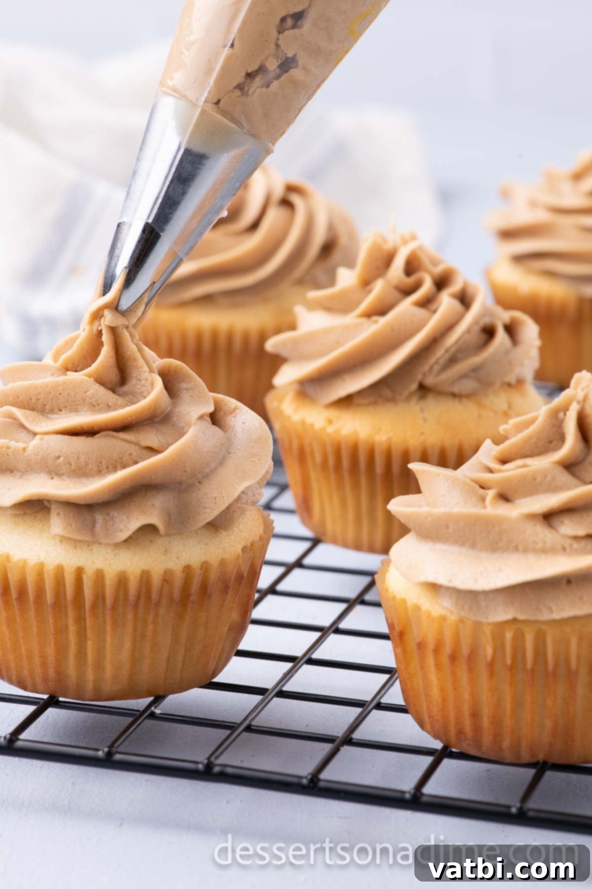 Decadent Salted Caramel Cupcakes 17 Salted caramel frosting being piped onto a cupcake, with additional caramel drizzle.