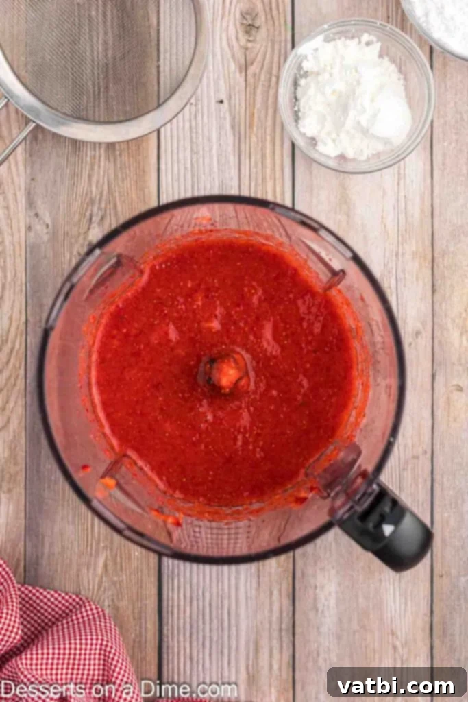Easy No-Bake Strawberry Cheesecake 5 Fresh, vibrant strawberries being blended in a food processor until completely pureed, creating a smooth and colorful base for the strawberry cheesecake filling.