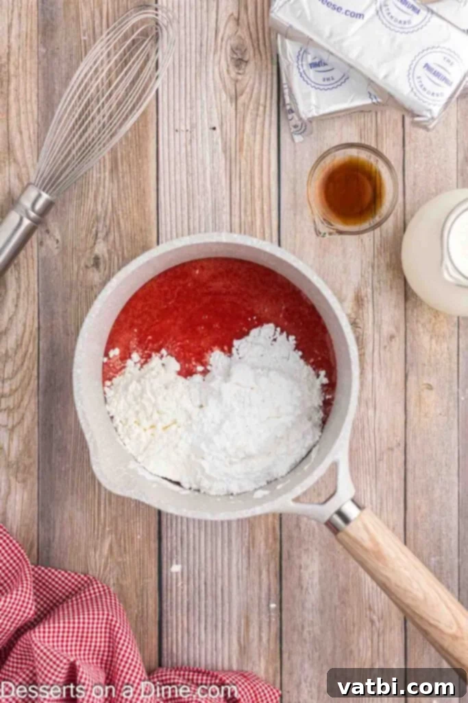 Easy No-Bake Strawberry Cheesecake 6 A small saucepan containing vibrant strawberry puree, powdered sugar, and cornstarch, being whisked together over medium heat to thicken, creating a flavorful base for the cheesecake.