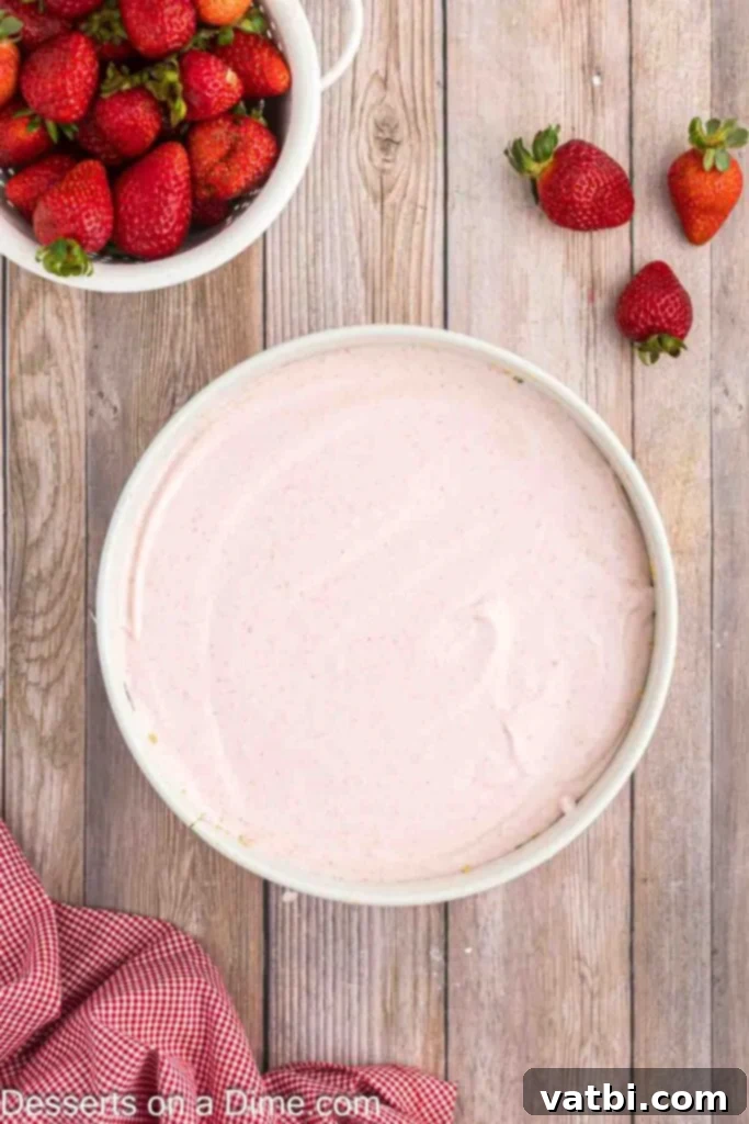 Easy No-Bake Strawberry Cheesecake 9 The finished, smooth and creamy no-bake strawberry cheesecake filling being poured into the chilled graham cracker crust in a springform pan, ready for refrigeration.