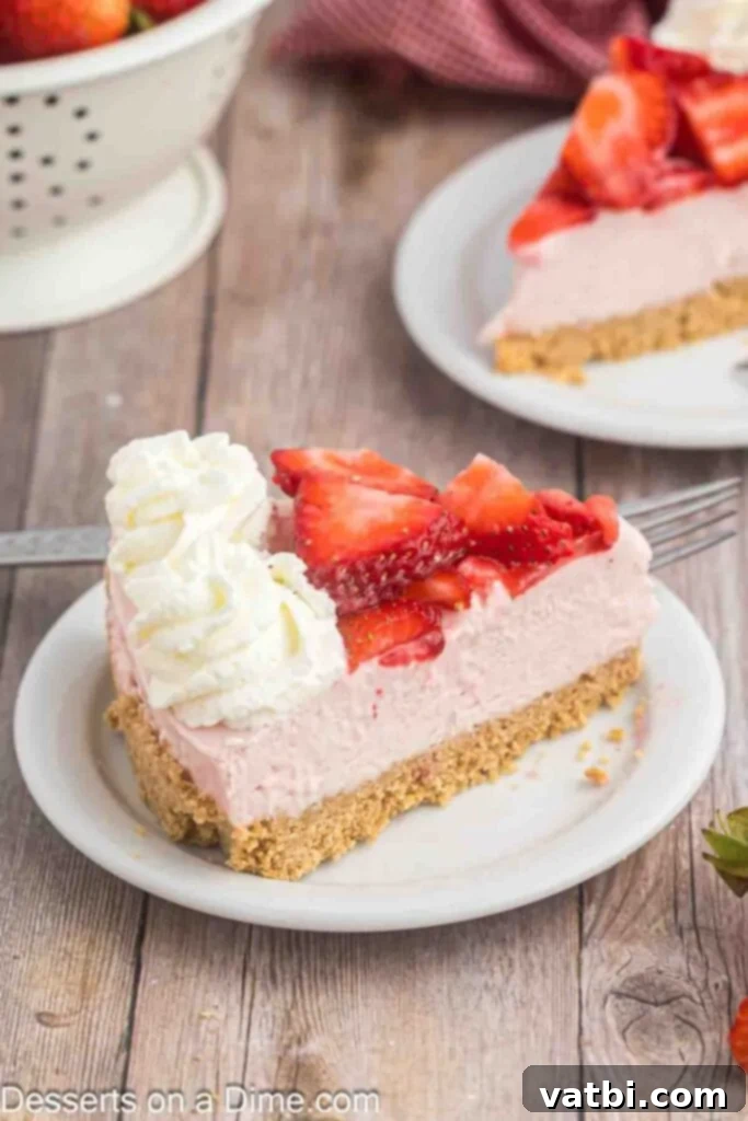 Easy No-Bake Strawberry Cheesecake 10 A perfect slice of no-bake strawberry cheesecake, adorned with fresh strawberry slices and a swirl of homemade whipped cream, elegantly placed on a white plate, ready to be enjoyed.