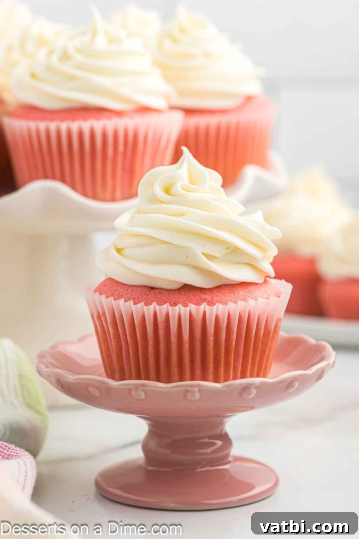 Blushing Velvet Cupcakes 2 A beautifully decorated pink velvet cupcake resting elegantly on a white pedestal, ready to be enjoyed.