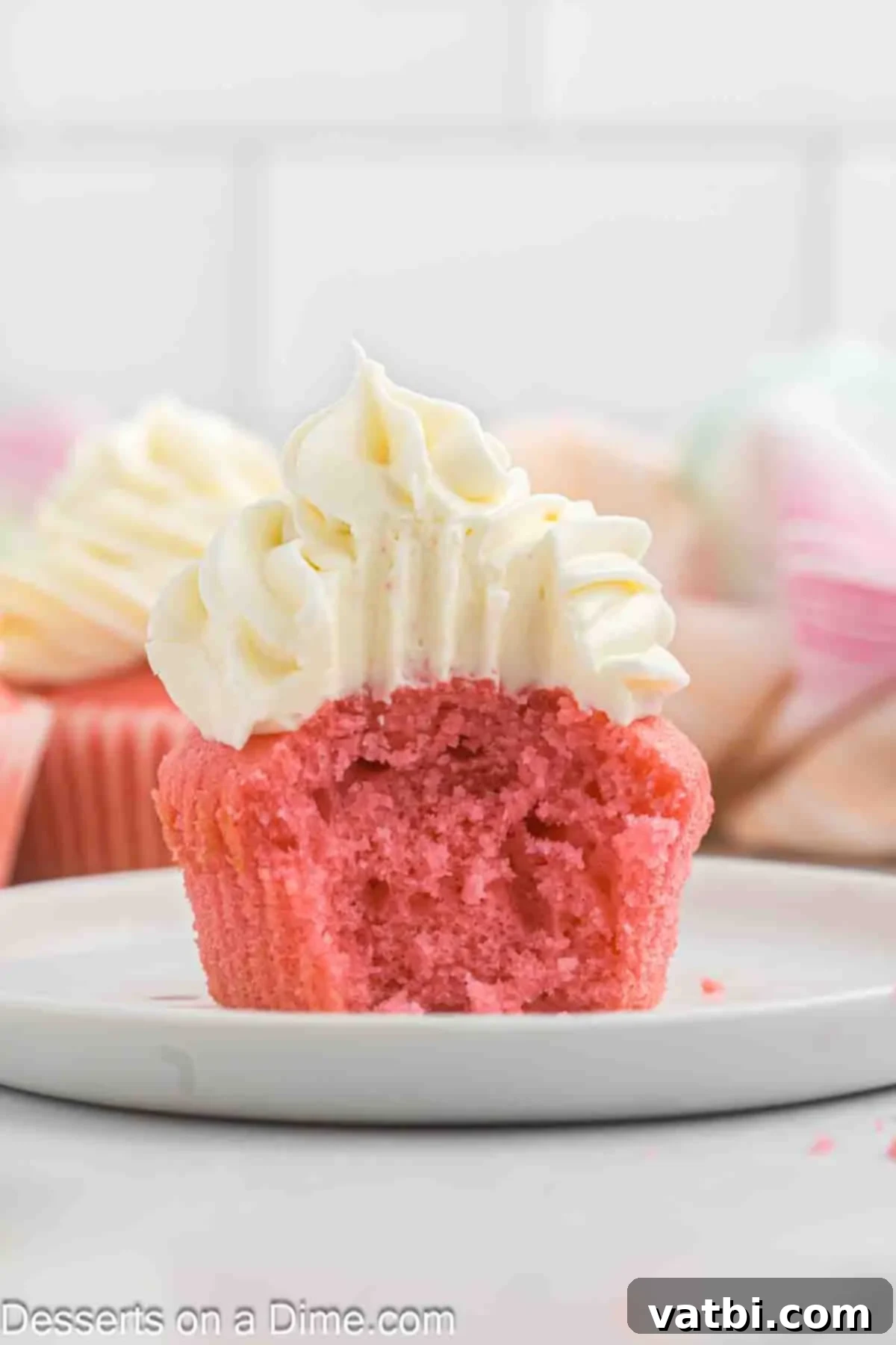 Blushing Velvet Cupcakes 12 A pink velvet cupcake cut in half on a plate, revealing its moist, tender crumb and the thick layer of cream cheese frosting.