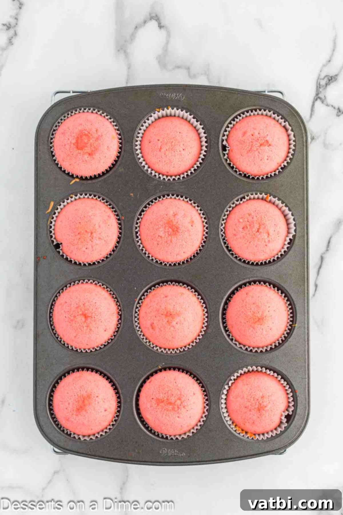 Blushing Velvet Cupcakes 8 Freshly baked pink velvet cupcakes in a muffin tin, cooling slightly before removal.