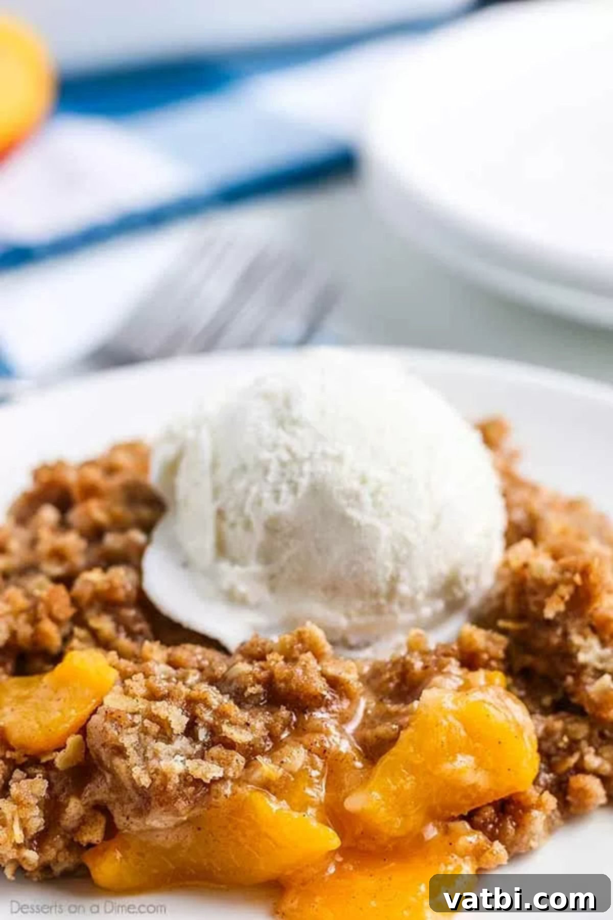 Easy peach crisp recipe is such a classic and delicious recipe. Sweet peaches, brown sugar and oatmeal crumble make this a decadent dessert that is so simple. This easy peach crisp with fresh peaches is the best recipe. #dessertonadime #easypeachcrisprecipe #desserts Peach Crisp on a white plate topped with vanilla ice cream, ready to be enjoyed.