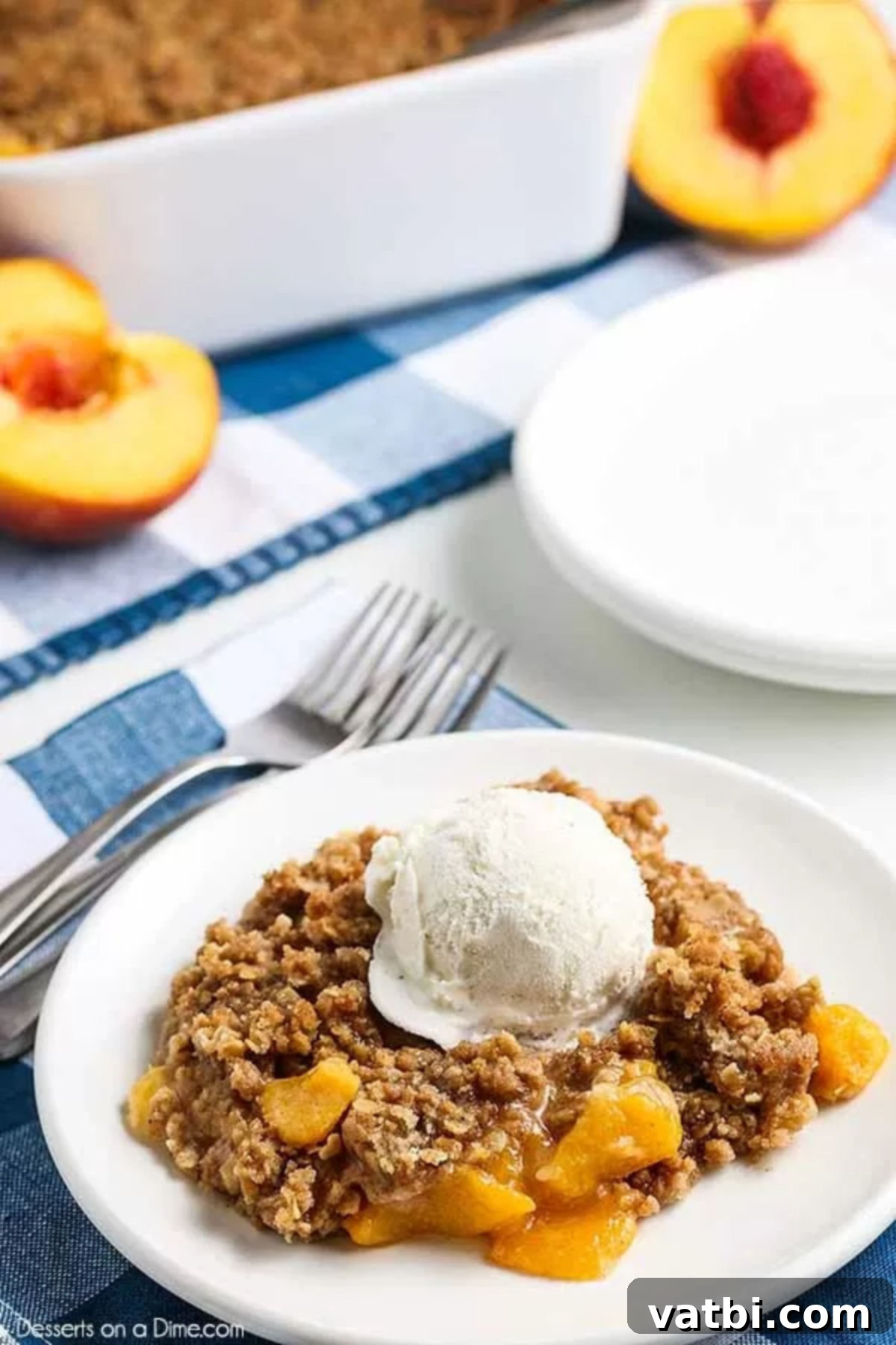 Easy peach crisp recipe is such a classic and delicious recipe. Sweet peaches, brown sugar and oatmeal crumble make this a decadent dessert that is so simple. This easy peach crisp with fresh peaches is the best recipe. #dessertonadime #easypeachcrisprecipe #desserts Close-up of a warm peach crisp on a white plate, topped with a scoop of melting vanilla ice cream and a fresh mint sprig.