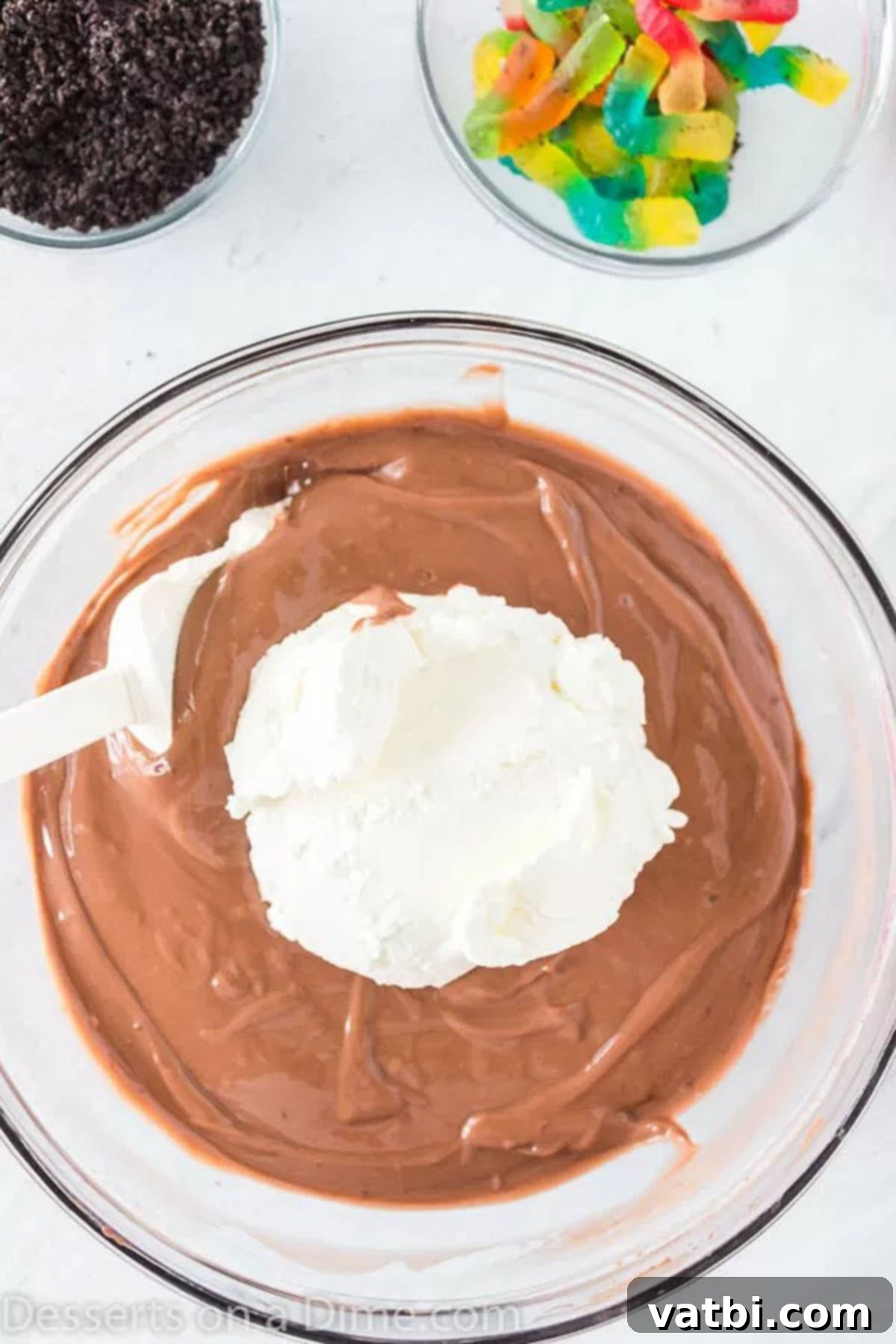 Ultimate Dirt Cup Delight 3 Thawed whipped topping being gently folded into the prepared chocolate pudding mixture with a spatula.