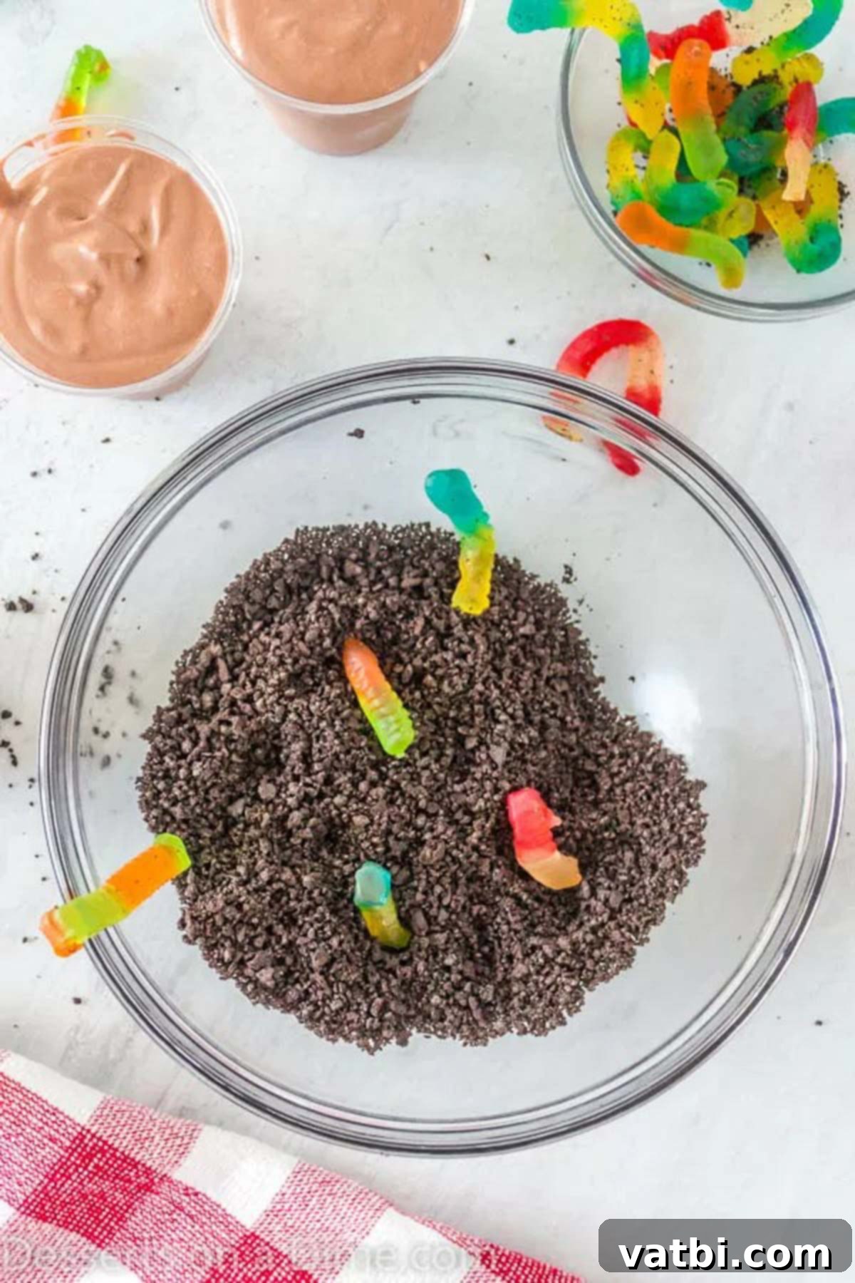 Ultimate Dirt Cup Delight 4 A bowl filled with finely crushed Oreo cookies and several colorful gummy worms, ready to be used as toppings.