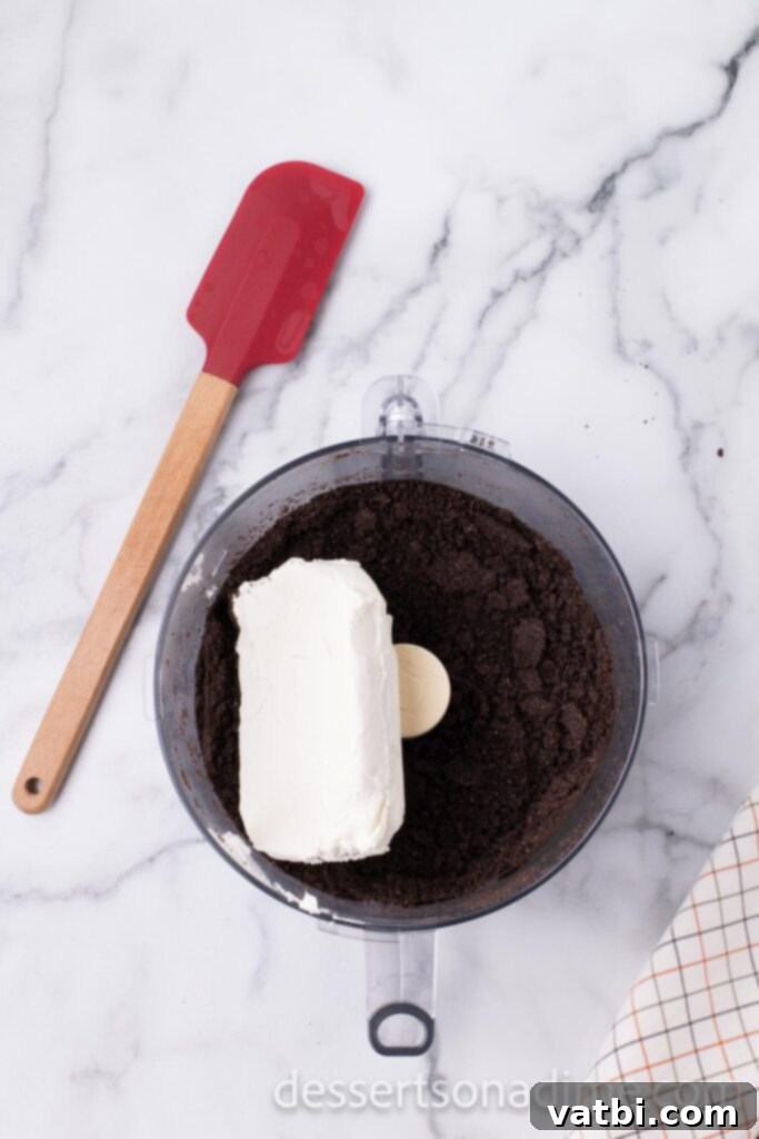 Touchdown Oreo Truffles 4 Softened cream cheese being added to the finely crushed Oreo cookies in a food processor.