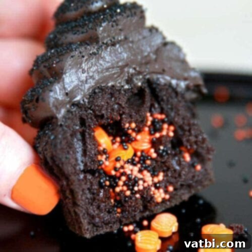 A hand holding a chocolate cupcake with orange sprinkles.