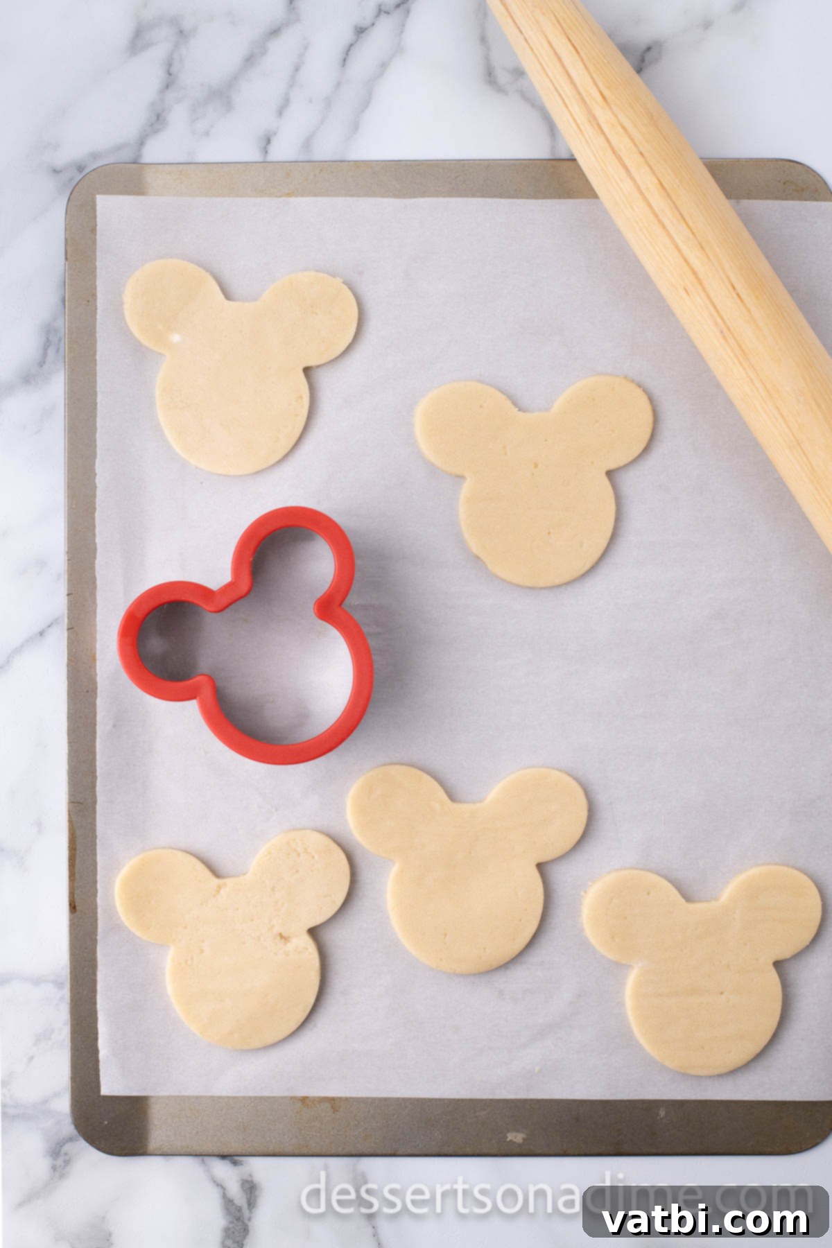 Magical Mickey Bakes 9 Mickey Mouse shapes cut out of cookie dough using a cookie cutter.