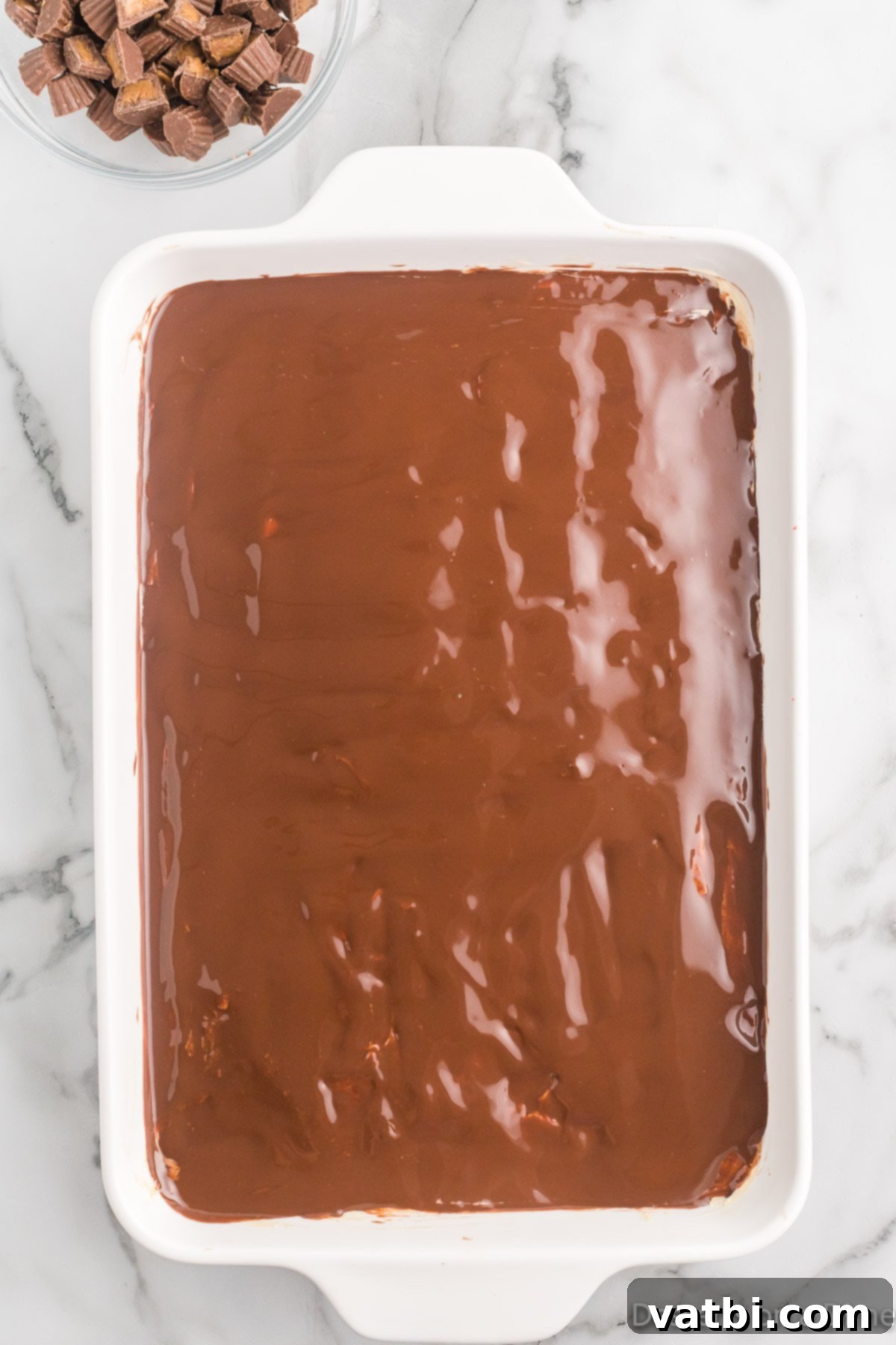No-Bake Peanut Butter Bliss 10 Chocolate Magic Shell topping being spread over the top layer of peanut butter filling.