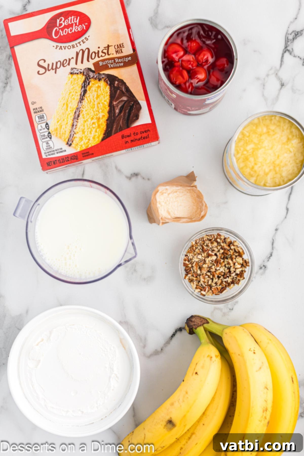 Party Punch Bowl Delight 3 A flat lay photograph displaying all the ingredients for Punch Bowl Cake: fresh bananas, a box of yellow cake mix, cans of crushed pineapple, instant pudding mix, milk, mixed nuts, and cherry pie filling.