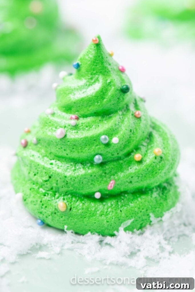 Sugar-Spun Christmas Trees 10 A single Meringue Christmas Tree cookie, perfectly piped and sprinkled, on a platter with a dusting of powdered sugar.