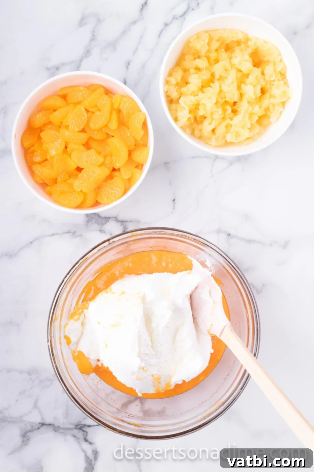 Tangerine Dream 7 Thawed whipped topping being gently folded into the orange Jell-O and pudding mixture with a spatula.