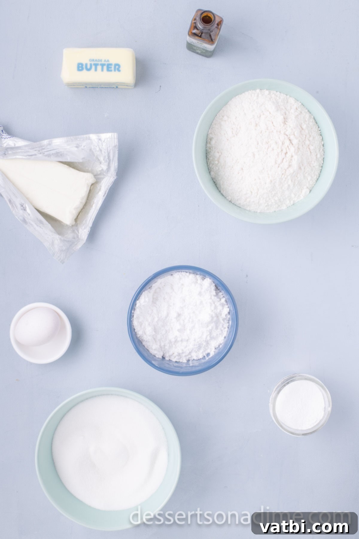 A selection of ingredients for the Ooey Gooey Butter Cookies recipe including butter, cream cheese, granulated sugar, flour, vanilla extract, and eggs.