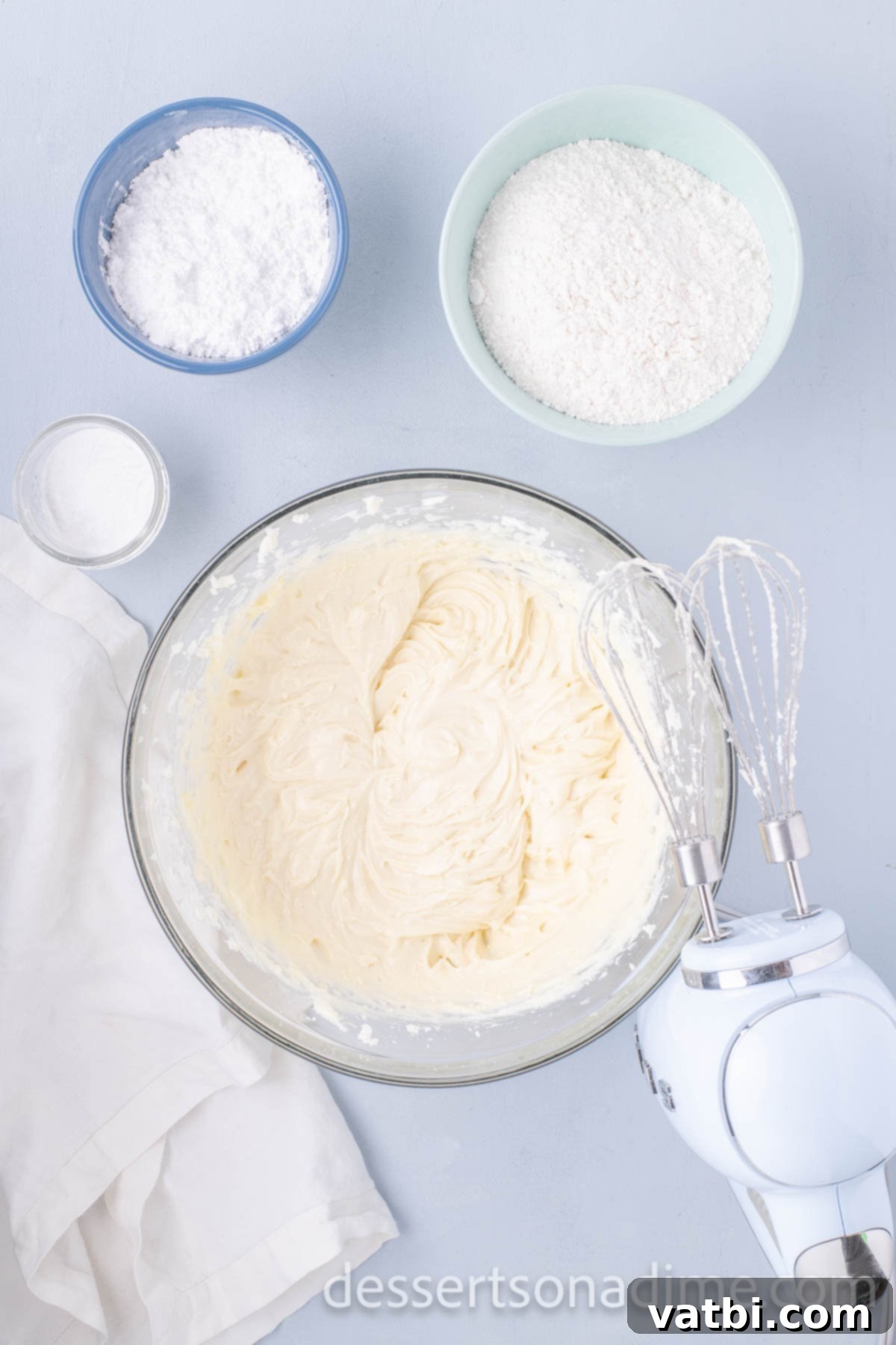 A bowl of softened cream cheese and butter being combined with an electric mixer.
